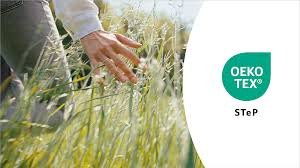 Hand touching tall grass with OEKO-TEX® STeP logo, symbolising sustainable and responsible textile production.