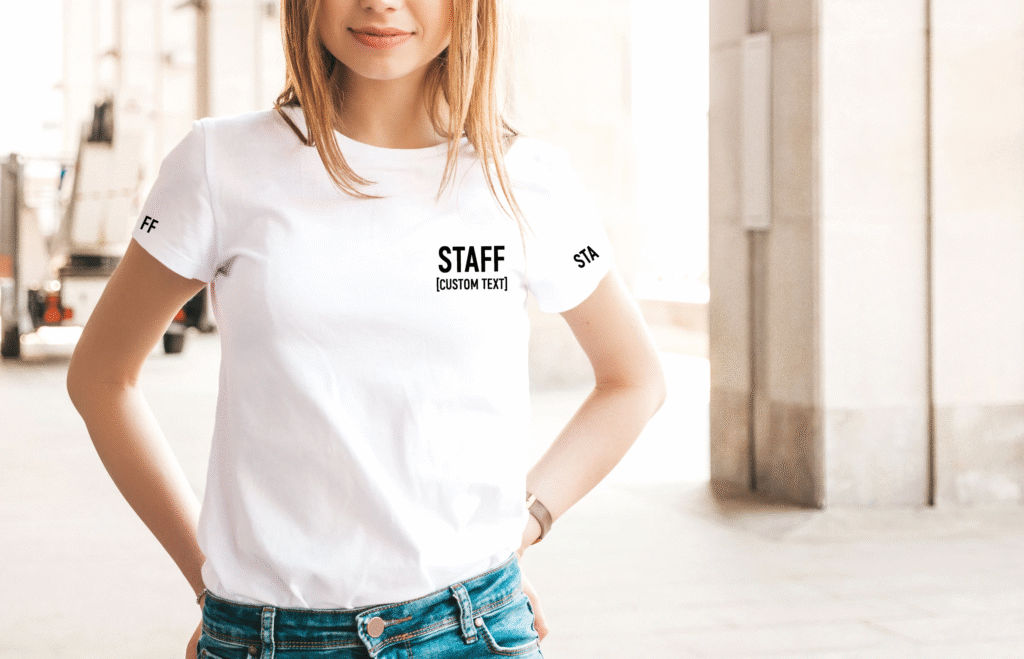 Mujer sonriente usando una camiseta blanca personalizada con la palabra 'STAFF' en un evento al aire libre.