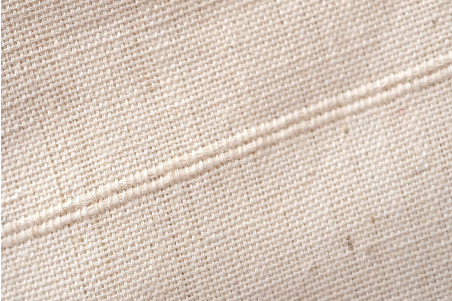 Detailed close-up of a beige woven linen fabric with visible weave pattern and seam.